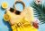 Vitalia Probiotic Cookie Dark Chocolate & Hazelnut styled in a vibrant summer setting with lemons, palm leaf, woven bag, sunglasses, and yellow skirt