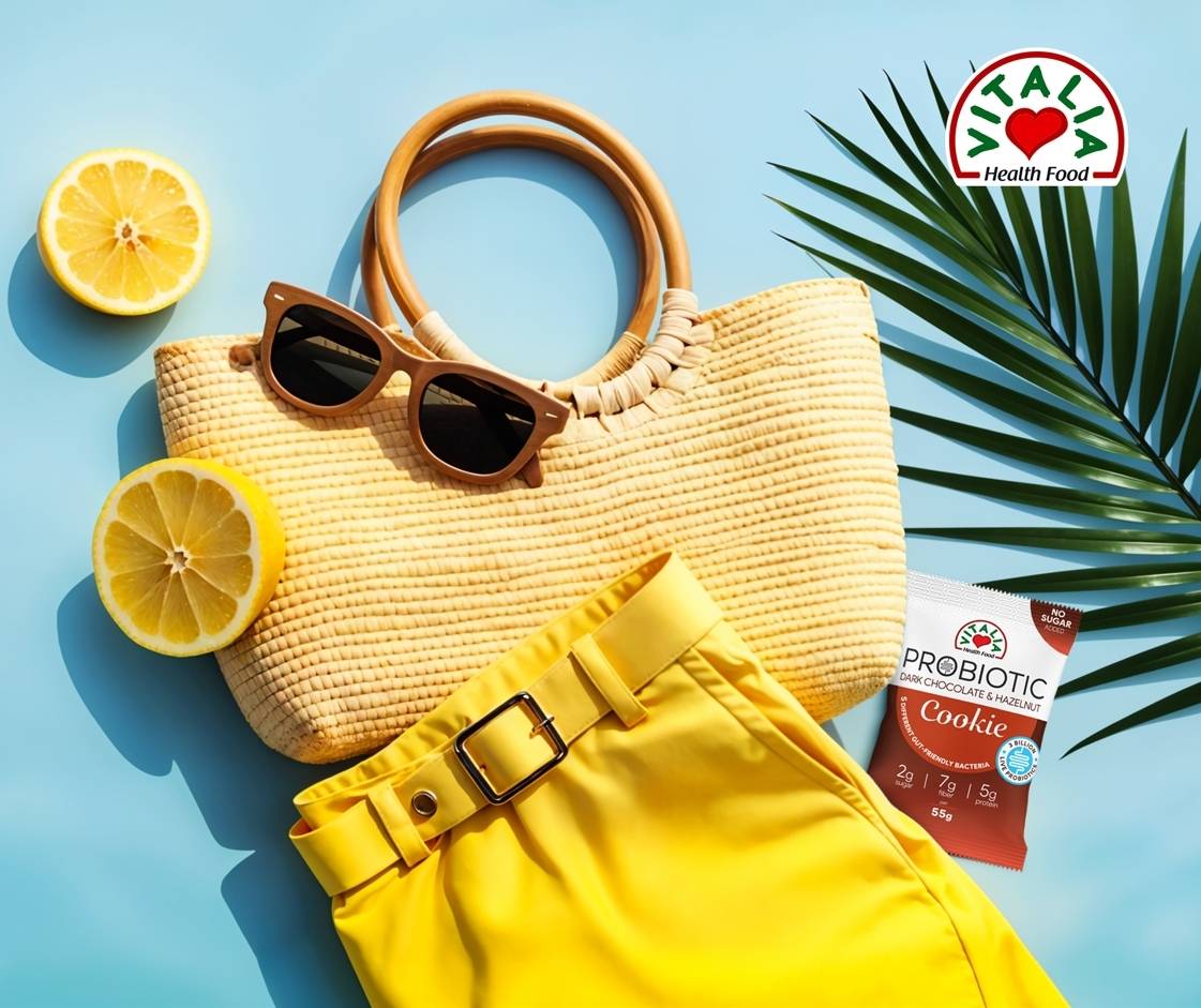 Vitalia Probiotic Cookie Dark Chocolate & Hazelnut styled in a vibrant summer setting with lemons, palm leaf, woven bag, sunglasses, and yellow skirt
